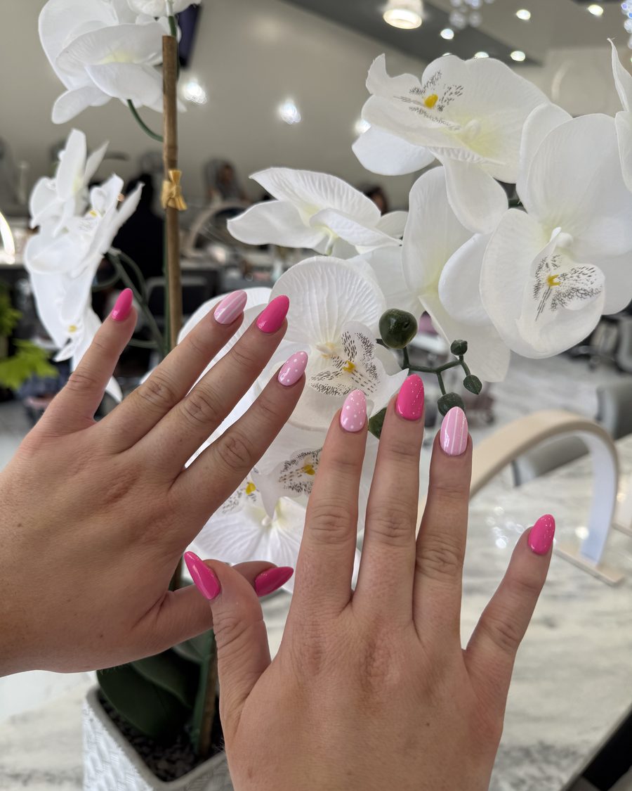 Almond-shaped gel manicure in two shades of pink, photographed in the salon beside white orchids